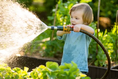 A child watering the garden with a hose, hopefully it isn't soft water that's bad for plants.