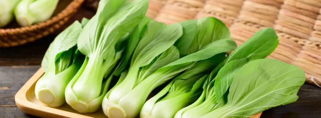 Fresh green bok choy on a wooden tray.