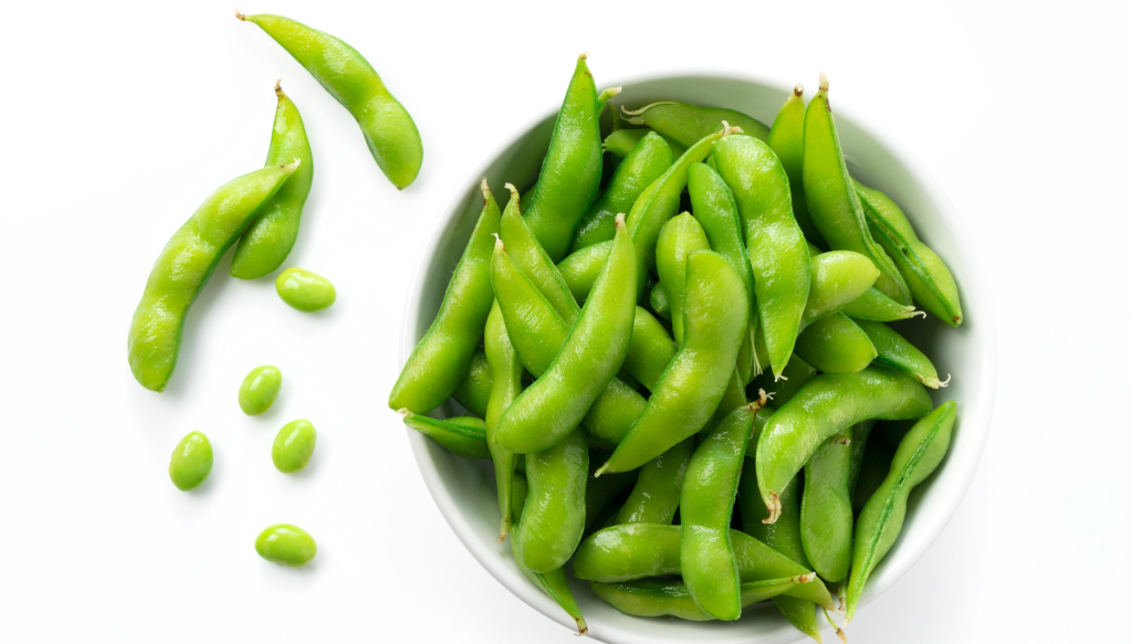 Green edamame seeds and pods in a white bowl.