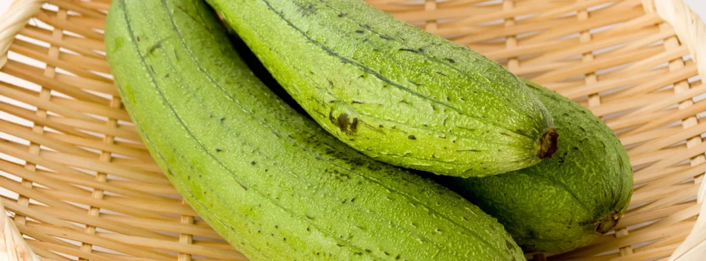 Green luffa gourds in a brown bamboo bowl.