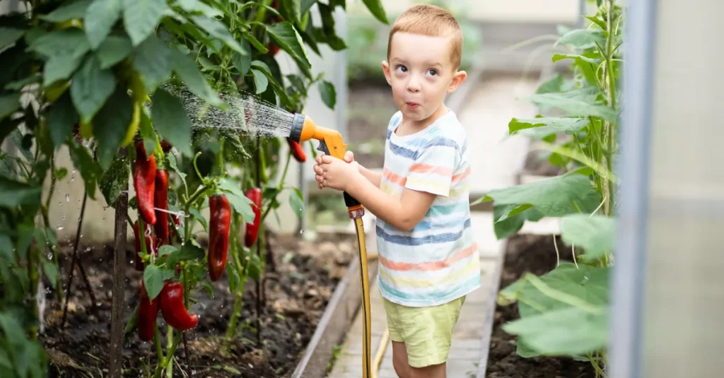 A young boy watering the garden with a hose.